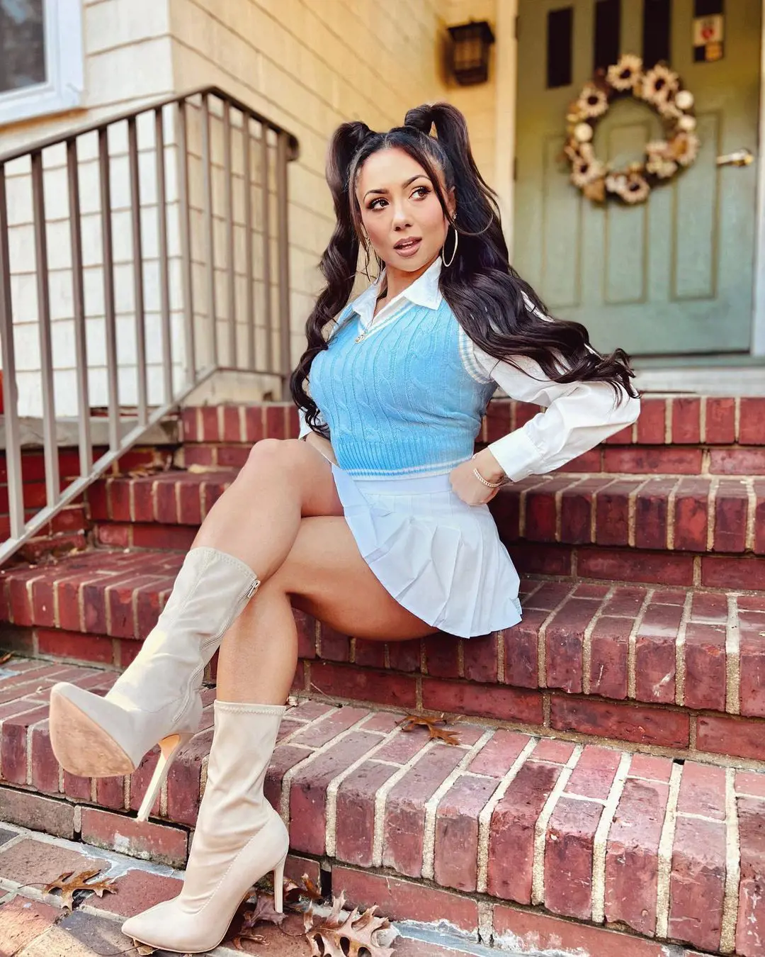 Ashley Nocera wearing blue top and white skirt posing on a staircase in November 2022