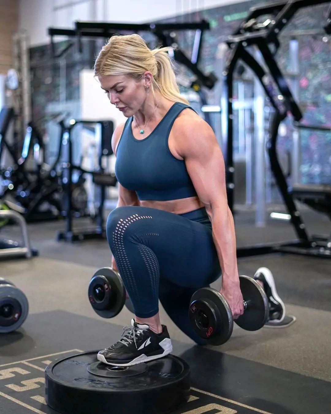 Brooke Ence performing Deficit Reverse Lunge holding two dumbbells in a gym in August 2021