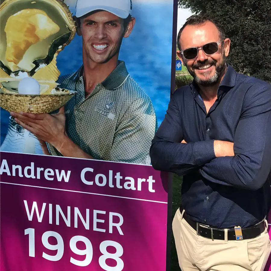 Andrew Coltart stands next to a photograph of himself as the inaugural champion of the Qatar Masters in 1998
